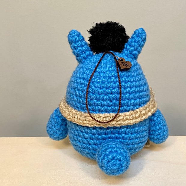 Crocheted blue chibi Totoro, wearing a cream colored scarf with a dust sprite on his head.