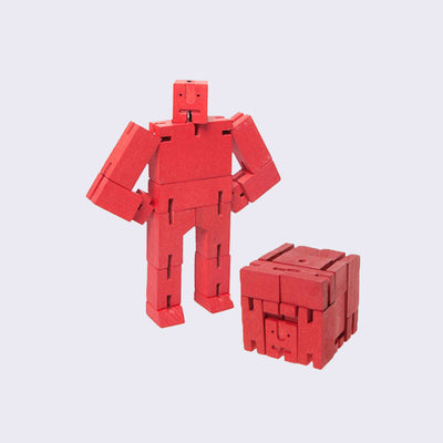 Wooden robot made out of many rectangular parts standing with its arms on its hips. The same robot is folded into a perfect cube shape in front.