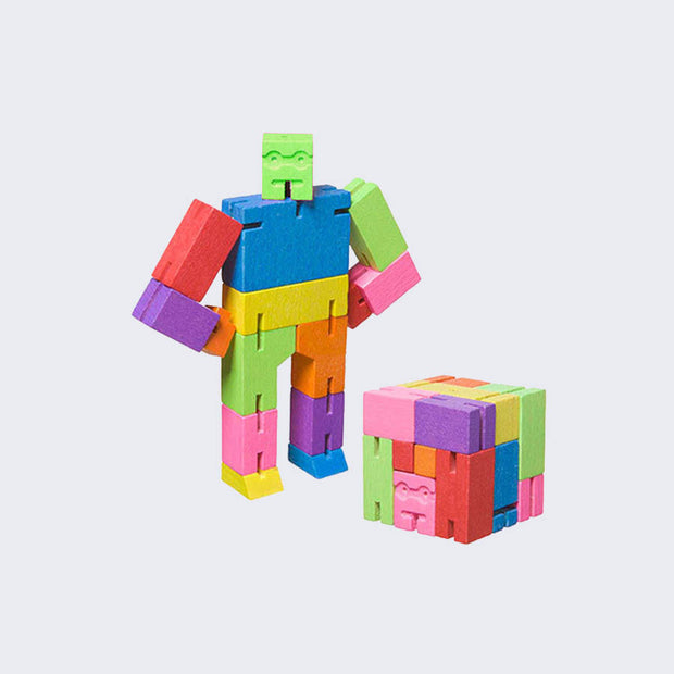 Wooden robot made of all different colored square-like shapes, standing with both arms on its hips. In front is the same robot, folded into the shape of a perfect cube. 
