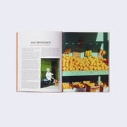 Open book spread featuring a page of text with the header "San Francisco." Next page features a photo of a fruit stand, filled with oranges and some bananas on the wall.