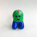 Small vinyl figure of a green round, bald creature with hollowed eyes and a single tooth mouth. It has pink veins on it and has human legs, which are in a kneeling position.