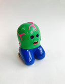 Small vinyl figure of a green round, bald creature with hollowed eyes and a single tooth mouth. It has pink veins on it and has human legs, which are in a kneeling position.