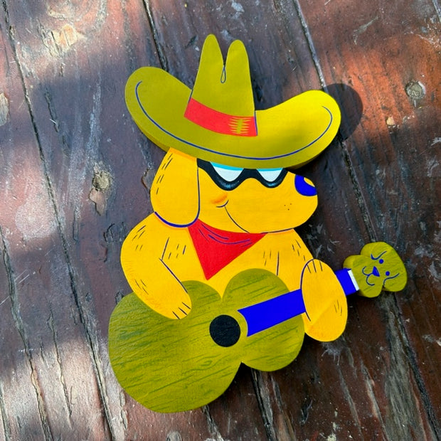 Wooden die cut sculpture of a yellow dog wearing a green cowboy hat and strumming a green guitar.