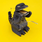 Carved wooden sculpture of a black Godzilla, standing with arms propped up, mouth open and crank on its stomach.