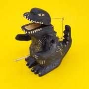 Carved wooden sculpture of a black Godzilla, standing with arms propped up and crank on its stomach.