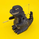 Carved wooden sculpture of a black Godzilla, standing with arms propped to its side and crank on its stomach.