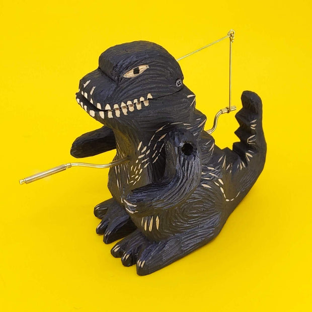 Carved wooden sculpture of a black Godzilla, standing with arms propped to its side and crank on its stomach.