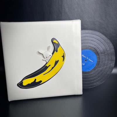 White vinyl fabric panel with a graphic Andy Warhol style browning banana with a small white bunny popping out of it. A record made out of vinyl fabric comes out of the white sleeve, with a blue label that says "Post It Show 18"