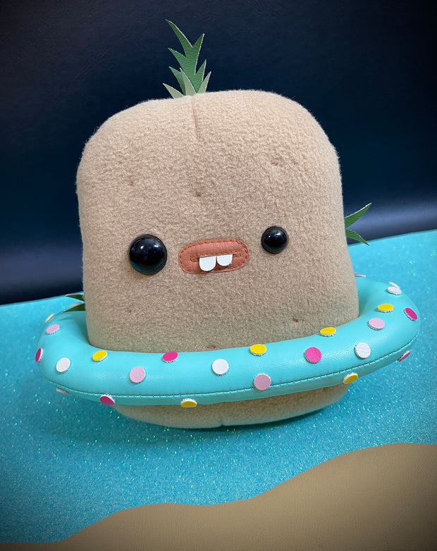 A light brown plush potato with mismatched eyes, buckteeth and sprouts growing from it. It has a blue and colorful polka dot pool ring floaty around its waist.