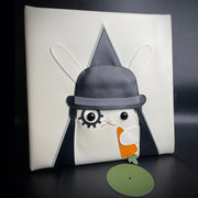 Vinyl (pleather) recreation of A Clockwork Orange's movie poster, featuring a white rabbit instead of a man, wearing a black bowler's hat, makeup over one eye and holding a carrot. A pleather vinyl album sits near the piece.