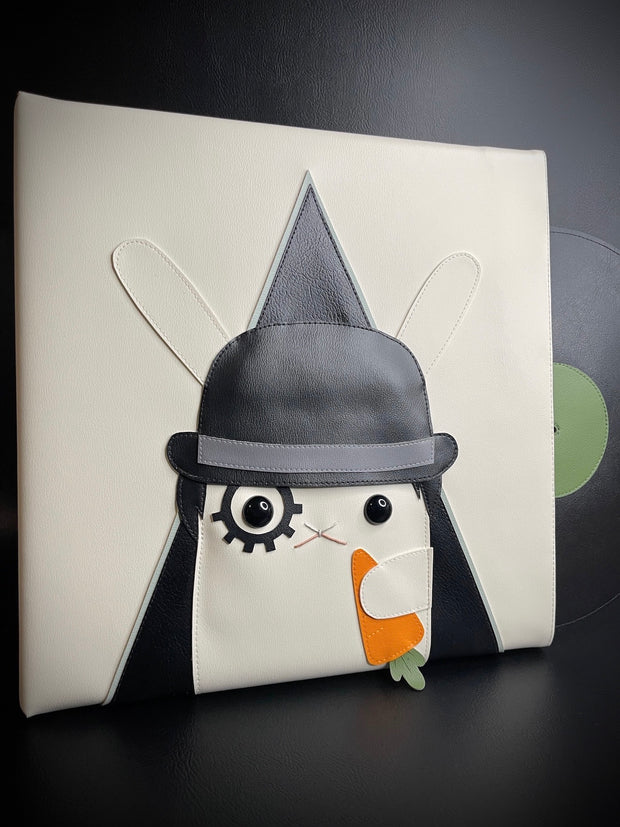 Vinyl (pleather) recreation of A Clockwork Orange's movie poster, featuring a white rabbit instead of a man, wearing a black bowler's hat, makeup over one eye and holding a carrot. A pleather vinyl album peeps out from the cover.