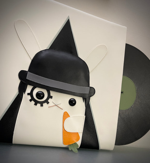 Vinyl (pleather) recreation of A Clockwork Orange's movie poster, featuring a white rabbit instead of a man, wearing a black bowler's hat, makeup over one eye and holding a carrot. A pleather vinyl album peeps out from the cover.