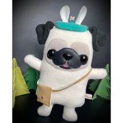 Plush sculpture of a pug, standing on 2 legs with its arms extended out. It wears a small crossbody satchel and a teal blue headband that has a small flower springing up from it.