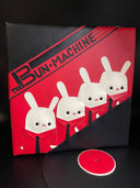  Vinyl (pleather) recreation of Kraftwerk's "The Man Machine" album cover, with a pleather album peeping out from the vinyl sleeve. Cover features 3 white bunnies, wearing matching red button ups and black ties with "The Bun Machine" written in black stylized font on a red background.