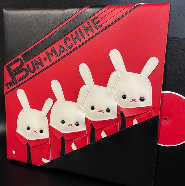 Vinyl (pleather) recreation of Kraftwerk's "The Man Machine" album cover, with a pleather album peeping out from the vinyl sleeve. Cover features 3 white bunnies, wearing matching red button ups and black ties with "The Bun Machine" written in black stylized font on a red background.