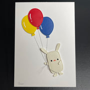 Vinyl sewn art piece, with slightly raised 3D elements of a small white rabbit holding a bundle of 3 balloons, blue, yellow and red.