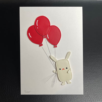 Vinyl sewn art piece, with slightly raised 3D elements of a small white rabbit holding a bundle of 3 red balloons.