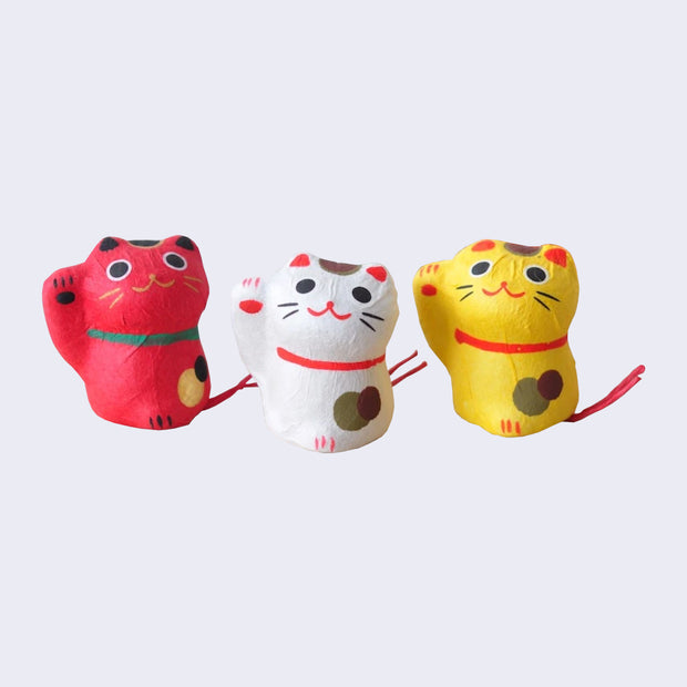 3 paper maché like figures, designed as traditional Japanese maneki, with spots, a collar and one paw raised up. Colors include red, white or yellow.