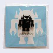 Metallic, gunmetal colored enamel pin of a robot with an angry expression and a white sparkle on its upper right chest. On a blue backing card.