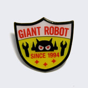 Enamel pin of a white, yellow and red shield shaped logo. "Giant Robot" is written in red across the top, there is a robot head in the middle with arms and "Since 1994" written underneath, above 3 red sparkles. 