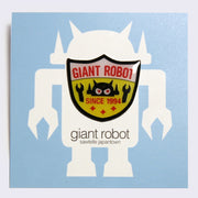Enamel pin of a white, yellow and red shield shaped logo. "Giant Robot" is written in red across the top. Pin is on a blue backing card.