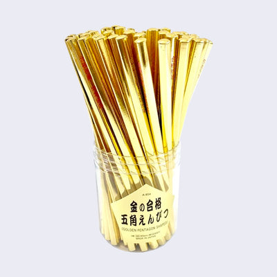 Clear cup holding numerous all golden unsharpened pencils. Cup has foreign writing on it.