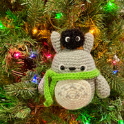 Round crochet Totoro with a green scarf and a dust sprite on its head. Totoro is strung onto a Christmas tree.