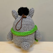 Back view of a round crochet Totoro wearing a green scarf with a dust sprite on his head.