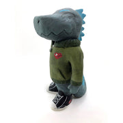 A painted clay sculpture of a happy looking grey blue Godzilla, with blue spikes and a long tail. He is wearing an army green jacket with a red dinosaur head logo and black sneakers.