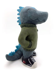 A painted clay sculpture of a happy looking grey blue Godzilla, with blue spikes and a long tail. He is wearing an army green jacket with a red dinosaur head logo and black sneakers. One hand is in his jacket pocket.