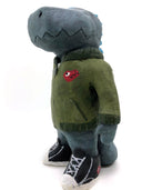 A painted clay sculpture of a happy looking grey blue Godzilla, with blue spikes and a long tail. He is wearing an army green jacket with a red dinosaur head logo and black sneakers.