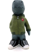 A painted clay sculpture of a happy looking grey blue Godzilla, with blue spikes and a long tail. He is wearing an army green jacket with a red dinosaur head logo and black sneakers. One hand is in his jacket pocket.