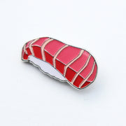 Enamel pin of a piece of tuna nigiri. A slice of striped tuna sitting atop white rice.