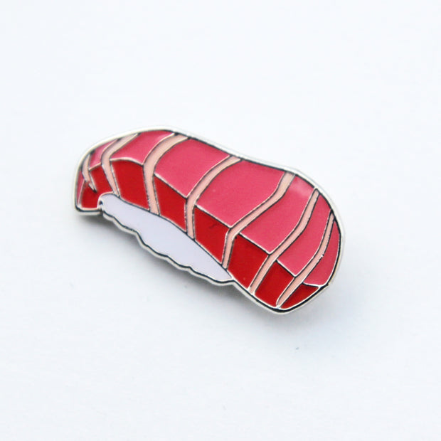 Enamel pin of a piece of tuna nigiri. A slice of striped tuna sitting atop white rice.