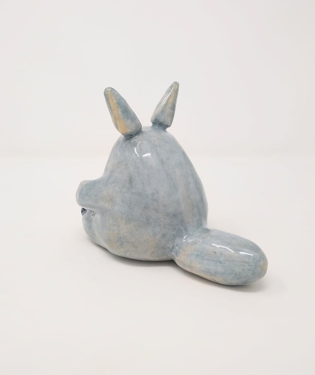 Glazed ceramic sculpture of Totoro, sitting and looking to the side curiously, with one paw slightly raised. He has a large, fluffy tail that lays flat behind him.