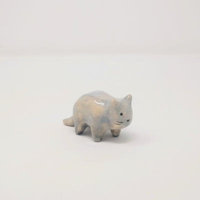 Small grey and white ceramic sculpture of a slightly chubby cat, standing on 4 legs with minimal shape details. It has a simplistic painted on cat face with whiskers.