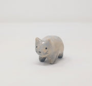 Small grey and white ceramic sculpture of a slightly chubby cat, standing on 4 legs with minimal shape details. It has a simplistic painted on cat face with whiskers.