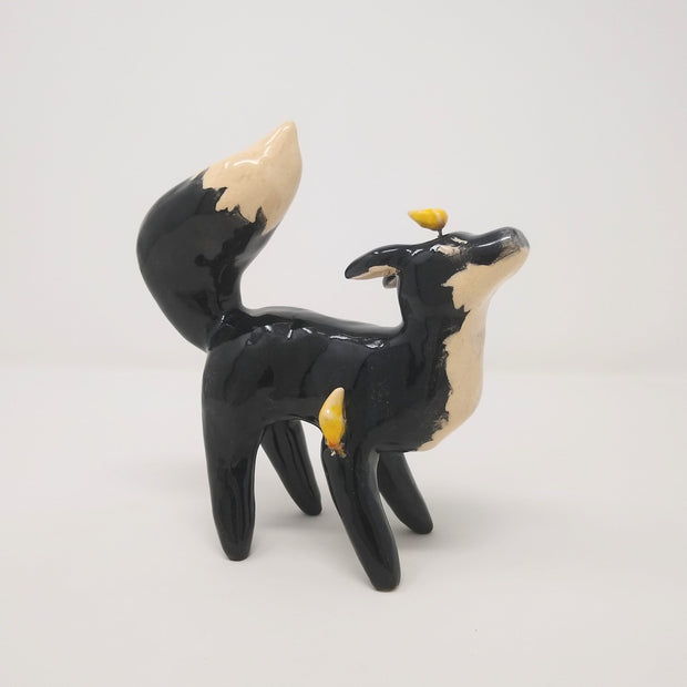 Ceramic sculpture of a black fox with white underbelly and tip of tail. It has non defined facial features and has a moon atop its head.