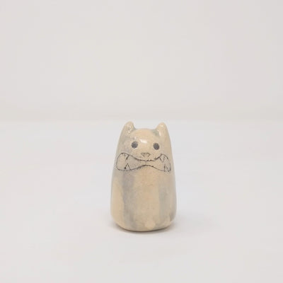 Small oval shaped cream color ceramic sculpture with little ears. It has a drawn on growling face.