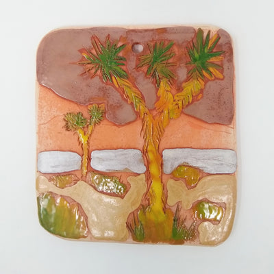Ceramic tile with design of 2 Joshua trees in a desert landscape.
