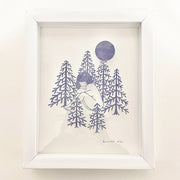 Cut lavender paper sculpture of a large girl with a bob haircut, sitting nude in the middle of a circle of abstract pine trees. A large moon looms overhead. Piece is mounted in a thick white wood frame.