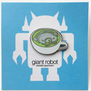 Enamel pin of a matcha latte in a shallow, white mug and a white bear design inside the cup. Pin is on a blue backing card.