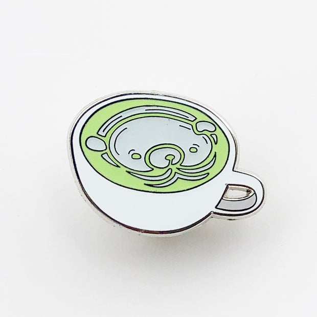 Enamel pin of a matcha latte in a shallow, white mug and a white bear design inside the cup.