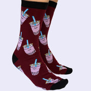 Side view of a model's feet wearing cartoon boba socks. The sock is burgundy but the boba cups are light purple. The heel and toe area is black.