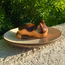 Sculpture of a sleeping tan cat, with simplistic facial features and a red smile. Cat has darker brown accent coloring towards the top of its body, with green flecks on its back to make it resemble a takoyaki.