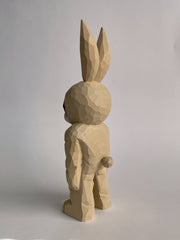 Whittled wooden sculpture of a golden eyed black cat with a white snout wearing a full body light tan bunny costume, with a pink belly and pink ears. It stands up on its legs with its arms straight to its side. It has a small round tail.