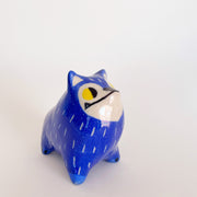 Ceramic sculpture of a blue furred dog, with pointy ears and a very unshapely body. It has yellow eyes and an underbite.