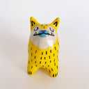 Yellow ceramic sculpture of a dog, with pointy ears and a very unshapely body. It has a blue nose, underbite and black lines drawn on its yellow fur.