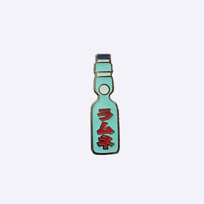 Enamel pin of a Japanese Ramune Soft Drink, a light blue bottle with a white ball towards the top and red Japanese script down the middle.