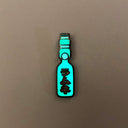 Enamel pin of a Japanese Ramune Soft Drink, a light blue bottle with a white ball towards the top and red Japanese script down the middle. Pin is glowing in the dark.